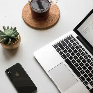 space gray iPhone X next to a turned-on laptop next to coffee and a succulent plant